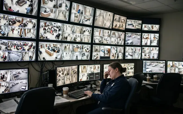 A control room with one operator facing a large wall of many CCTV feeds