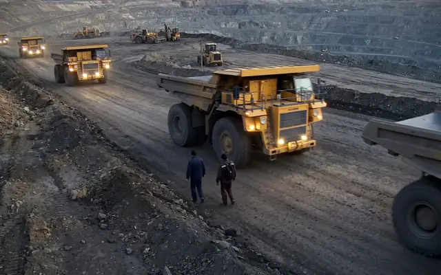 A worker in plain clothes without a hi-vis vest standing near a moving wheel loader