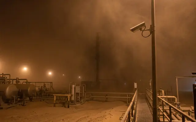 A large industrial site at night with only a few pools of light and large dark areas