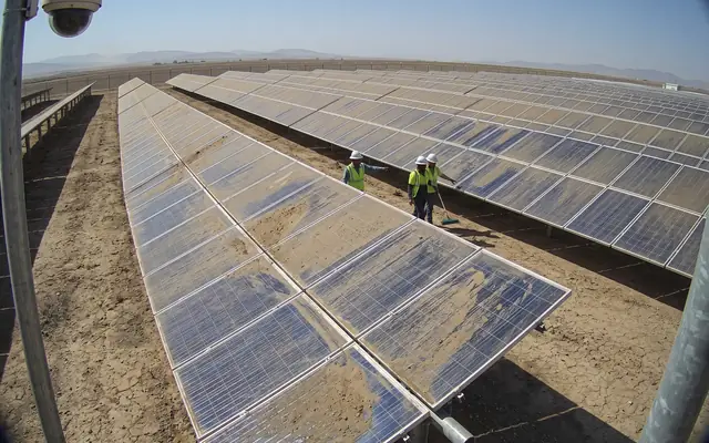A PV array in a dusty desert field with a thick grey dust layer on the modules