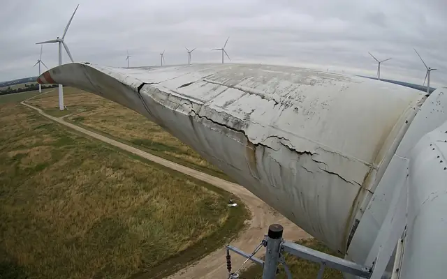 A close-up drone view of a wind turbine blade with a visible crack near the trailing edge