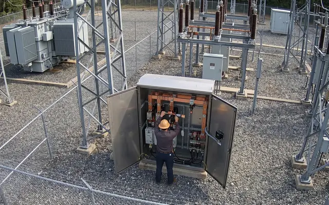 A worker in normal coveralls racking a live breaker, exposing the team to an arc-flash hazard