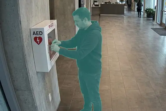 AI segmentation mask on a person tampering with an AED cabinet in a building lobby