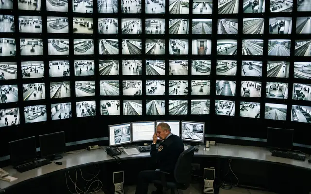 A control room with one operator facing a large wall of many CCTV feeds
