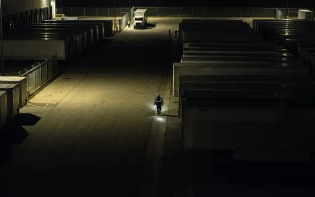 A large industrial site at night with only a few pools of light and large dark areas