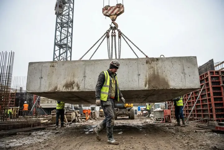 A worker walking directly underneath a heavy load suspended from a tower crane
